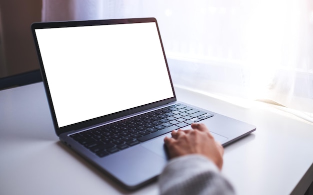 Mockup-Bild einer Geschäftsfrau, die das Touchpad eines Laptops mit einem leeren weißen Desktop-Bildschirm auf dem Tisch verwendet und berührt