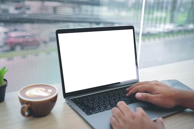 Foto mockup-bild einer geschäftsfrau mit einem laptop mit leerem weißen desktop-bildschirm mit kaffeetasse auf einem holztisch im café