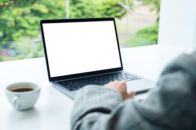 Mockup-Bild einer Hand, die ein Laptop-Touchpad mit einem leeren weißen Desktop-Bildschirm im Büro verwendet und berührt