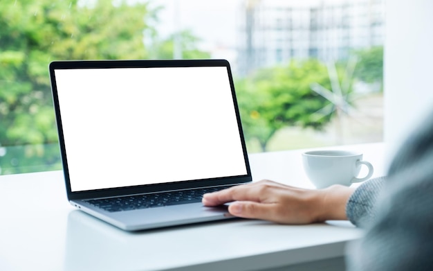 Mockup-Bild einer Hand, die ein Laptop-Touchpad mit einem leeren weißen Desktop-Bildschirm im Büro verwendet und berührt