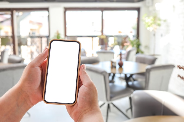 Mockup-Bild von Frauenhänden, die ein weißes Handy mit leerem Bildschirm im Café halten