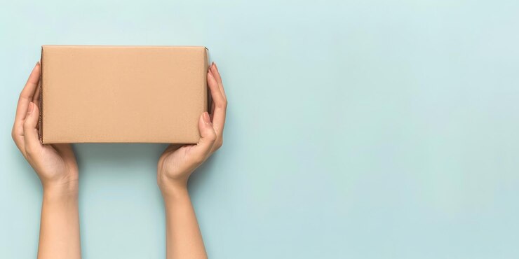 Mockup de caja de paquetes con la mano de una mujer en fondo azul para embalaje, entrega de compras, concepto de regalo.