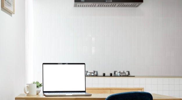 Mockup de una computadora portátil de pantalla blanca en una mesa de madera en la cocina