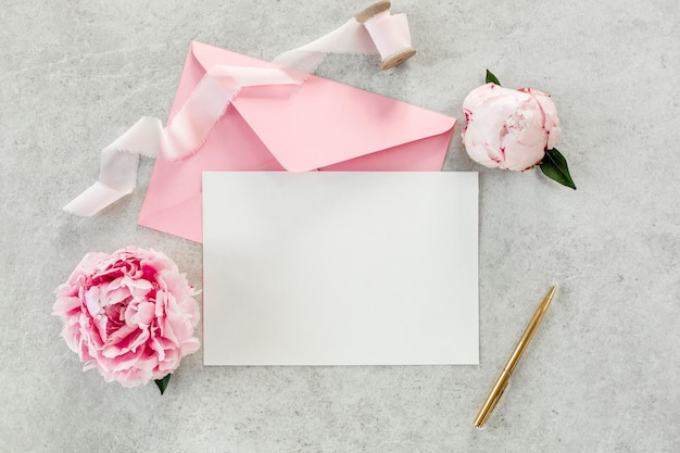 Mockup convite papel em branco cartão de saudação envelope rosa e peônias em flor de mesa de pedra cinza