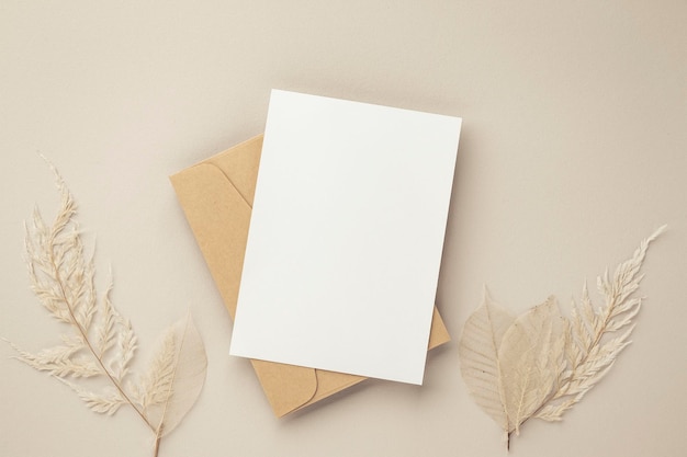 Mockup de convite de cartão de saudação em branco 5x7 em envelope marrom com flores secas em maquete plana de fundo bege