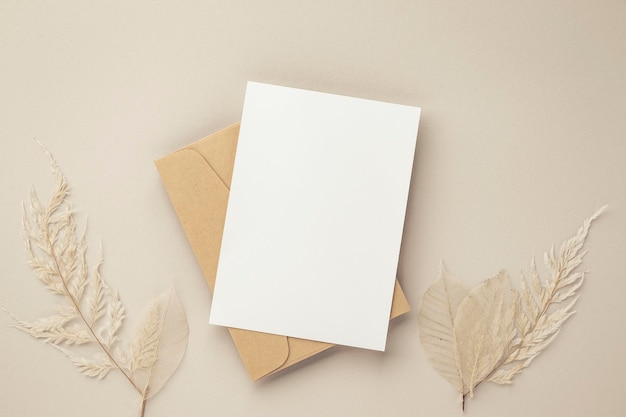 Foto mockup de convite de cartão de saudação em branco 5x7 em envelope marrom com flores secas em maquete plana de fundo bege