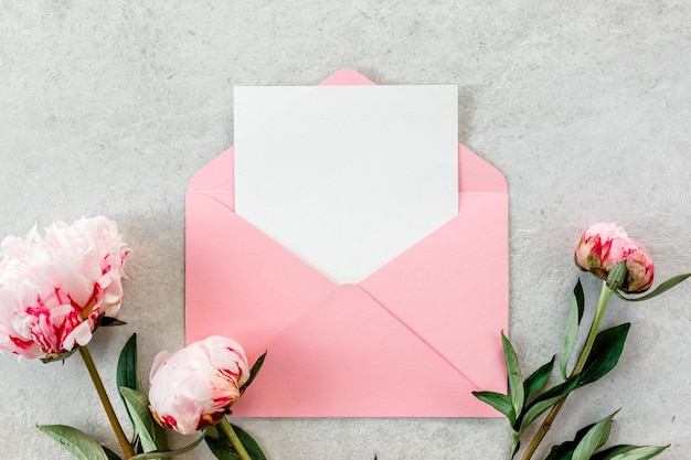 Mockup de convite papel em branco cartão de saudação envelope rosa e peônias em mesa de pedra cinza fundo de flor vista superior plana