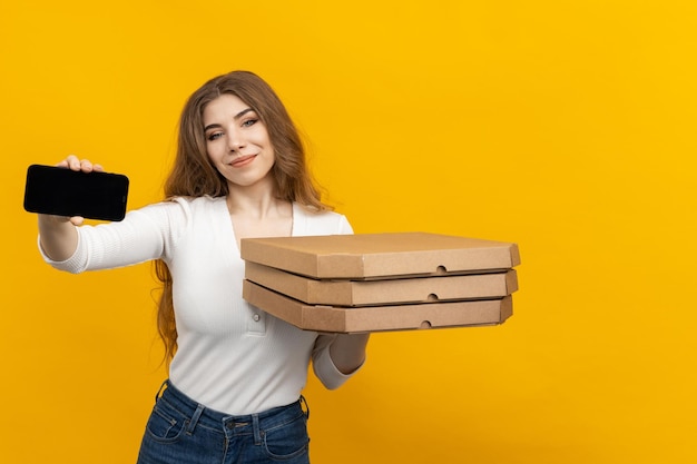 Mockup Una joven mujer sonriente con un teléfono inteligente y cajas de pizza sobre un fondo amarillo Pedir pizza a domicilio Entrega