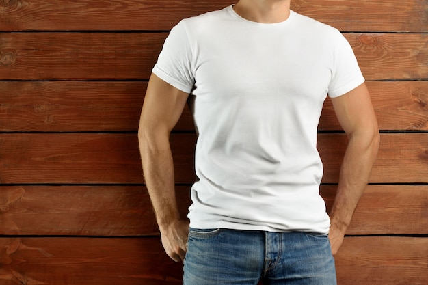Mockup-Kleidung. Athletischer fitter Kerl in einem leeren T-Shirt und in einer blauen Jeans auf einem braunen hölzernen Studiohintergrund. Vorlage bereit für Ihre Präsentation.