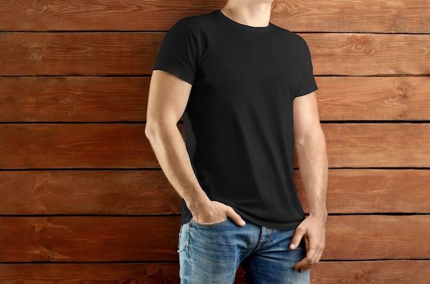 Mockup-Kleidung. Kräftiger schlanker Mann in schwarzem T-Shirt und Blue Jeans auf braunem Holzstudiohintergrund. Vorlage bereit für Ihre Präsentation.
