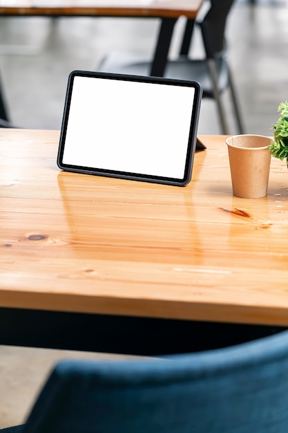 Mockup leere weiße Bildschirmtablette auf Holztisch im Caféraum, vertikale Ansicht.