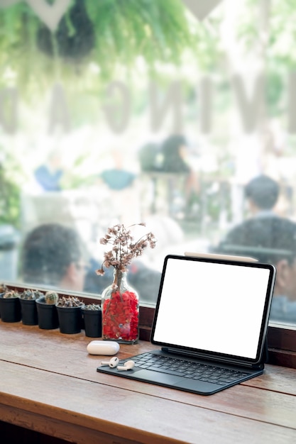 Mockup leere weiße Bildschirmtablette mit magischer Tastatur auf Holztisch im Café-Raum.