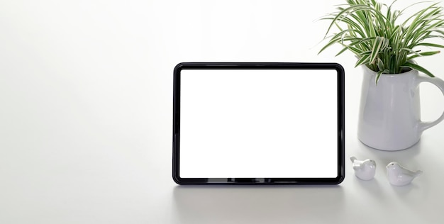 Mockup leerer weißer Bildschirm tragbares Tablet und Zimmerpflanze auf weißem Tisch mit Kopierraum.