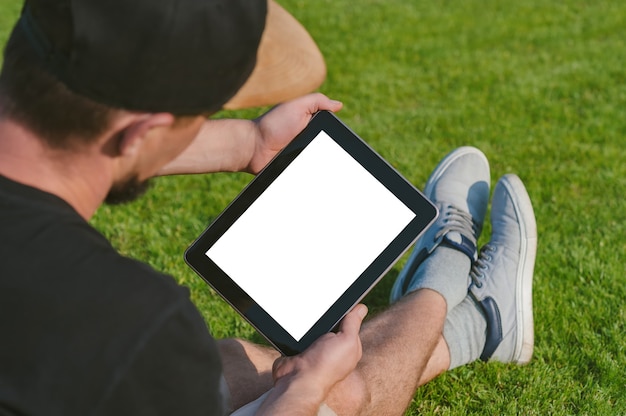 Foto mockup-tablet in den händen des kerls. vor dem hintergrund eines grünen rasens.