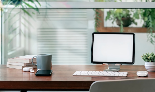 Mockup-Tablette mit leerem Bildschirm auf Ständer mit Tastatur auf Holztisch im Wohnzimmer, Home-Office-Konzept.