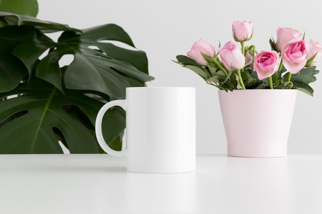 Mockup de taza con rosas rosadas en una maceta y una planta monstera