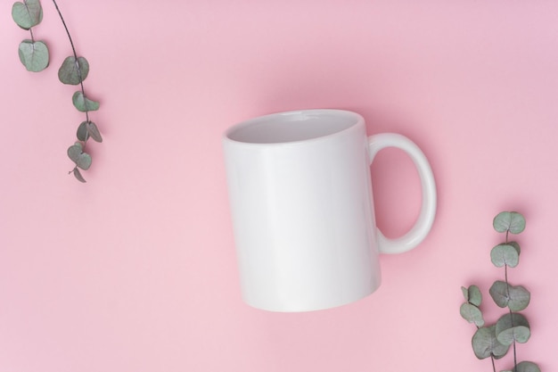 Mockup weiße Kaffeetasse oder Becher auf rosafarbenem Hintergrund mit Kopierraum. Leere Vorlage für Ihr Design, Branding, Geschäft. Echtes Foto. Eukalyptuszweige. Flach lag niemand