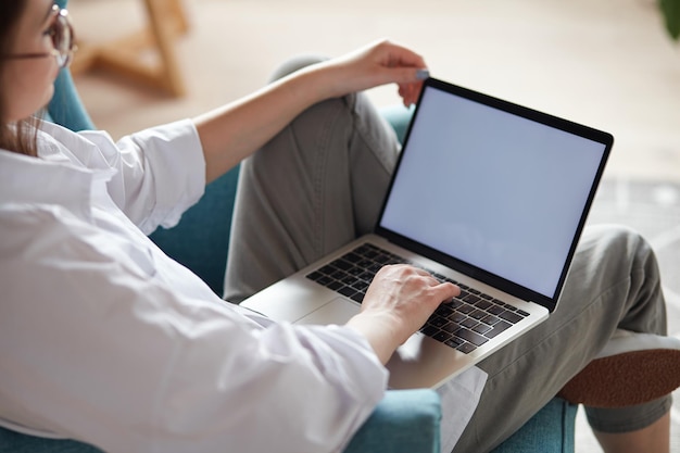 Mockup White Screen Laptop Frau mit Computer sitzt auf Sessel zu Hause Rückansicht Fokus auf Geröll