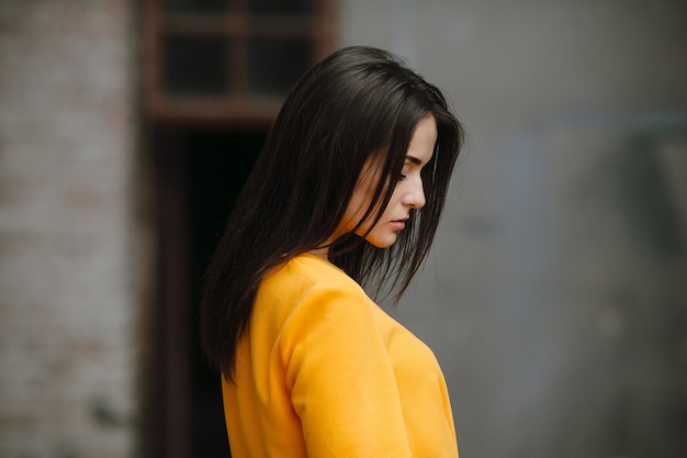 Moda atraente mulher em vestido laranja posando perto de uma parede branca