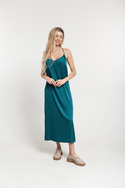 Moda bastante elegante modelo de mujer sonriente feliz con peinado rubio en vestido turquesa largo vintage con zapatos se encuentra sobre un fondo blanco en el estudio