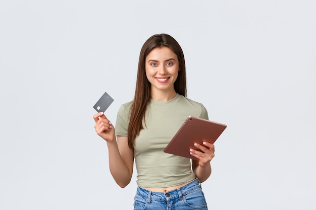 Moda y belleza, estilo de vida y concepto de compras, sonriente, apuesto cliente femenino, haciendo pedidos en línea con tarjeta de crédito y tienda de tableta digital en pared blanca de internet