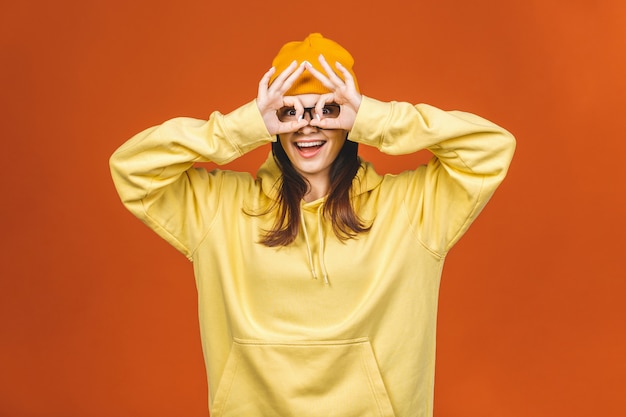 Moda bonita caucasiana jovem aluna vestindo roupas elegantes, rindo, apontando o dedo. Isolado sobre a laranja.