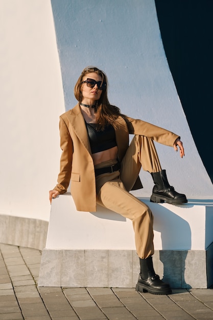 Moda de calle, atuendo casual y moderno para mujeres. Mujer en traje pantalón, camiseta sin mangas de cuero y botas ásperas al aire libre.