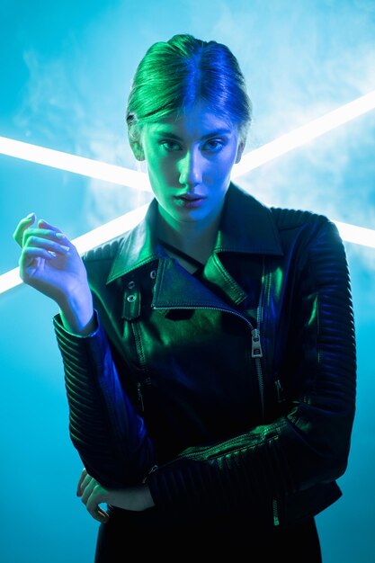 Moda cyberpunk Gente de luz de neón Estilo urbano futurista Retrato de color verde azul de mujer arrogante en chaqueta de cuero negro sobre fondo brillante de lámpara LED de humo blanco