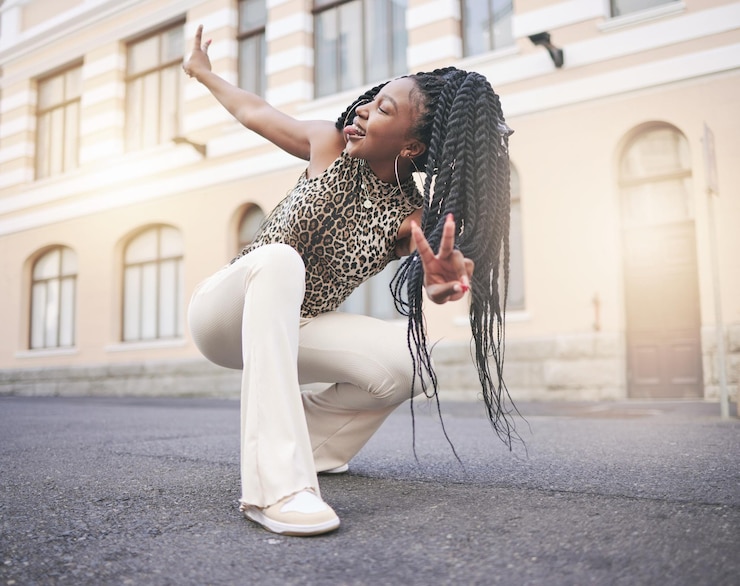 Foto moda de rua de mulher negra e mão de sinal de paz na cidade agachada e língua para fora em auto-expressão única garota criativa e urbana da geração z moderna e legal da nigéria com roupas de grife elegantes