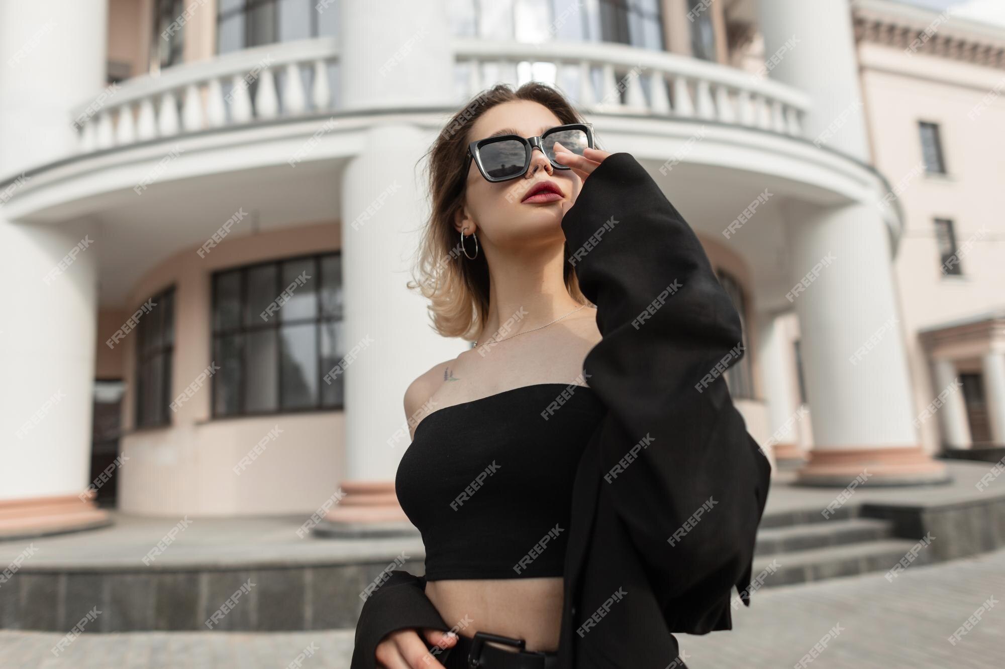 Moda de mujer bonita con ropa negra elegante y moderna con top y blazer usa gafas de sol modernas y frescas y camina la ciudad traje de estilo de