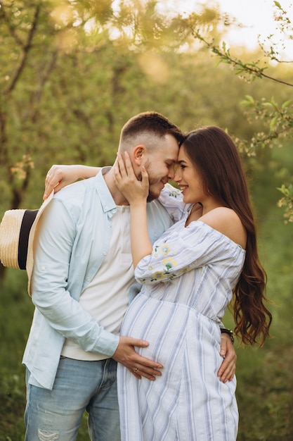 Moda y elegante mujer embarazada feliz y su esposo vistieron un tono blanco y azul pastel en el jardín en la puesta de sol