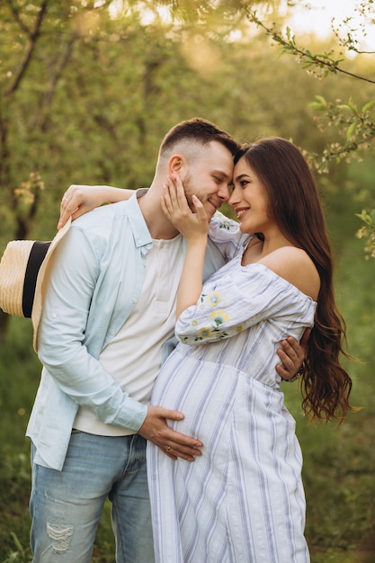 Moda y elegante mujer embarazada feliz y su esposo vistieron un tono blanco y azul pastel en el jardín en la puesta de sol