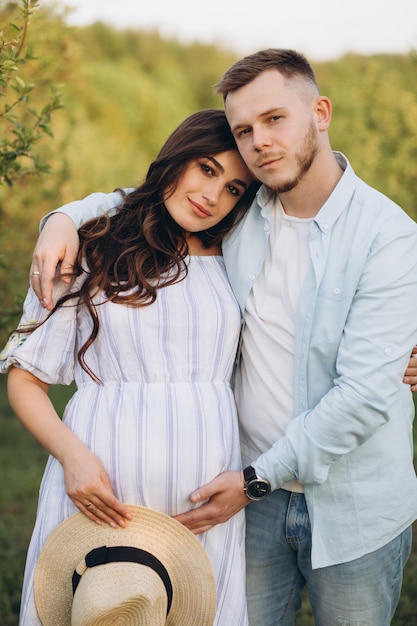 Moda y elegante mujer embarazada feliz y su esposo vistieron un tono blanco y azul pastel en el jardín en la puesta de sol