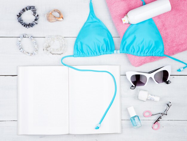 Moda feminina de verão com maiô azul livro toalha rosa cosméticos maquiagem bijou e fundamentos