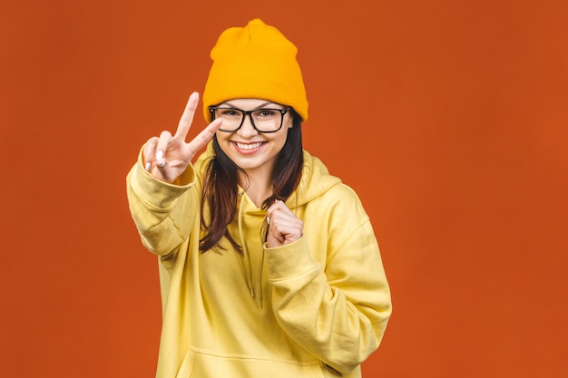 Moda hermosa joven caucásica joven estudiante vistiendo ropa elegante riendo, señalando con el dedo. Aislado sobre naranja.