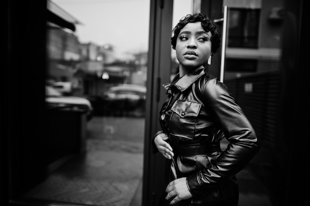 Moda hermosa mujer afroamericana posando en chaqueta de cuero negro en la calle.