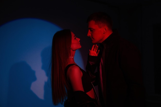 Moda hermosa pareja hombre y mujer bonita en ropa elegante negra sobre un fondo oscuro con luz roja y azul creativa en el estudio