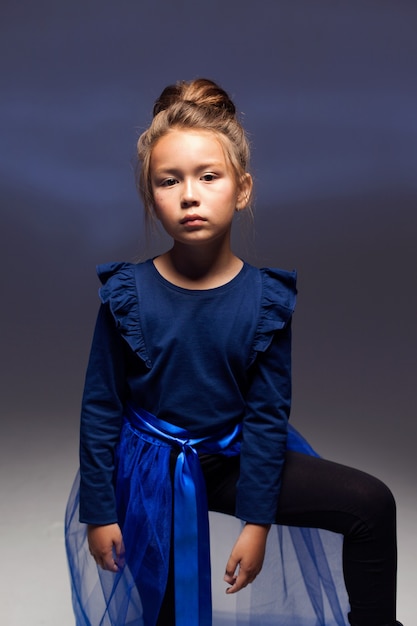 Moda infantil. Una linda niña de siete años con chaqueta, leggings y un tren azul posa sobre un fondo oscuro. Una foto de estudio. Moda