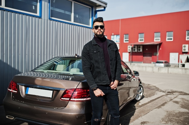 Moda jovem barbudo posando ao ar livre com carro grande