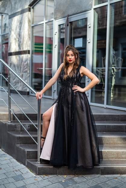 Moda jovem de comprimento total em vestido de noite preto, andando na cidade durante o dia. estilo de rua