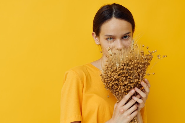 Foto moda jovem e bonita em buquê de flores secas de camiseta amarela posando fundo amarelo