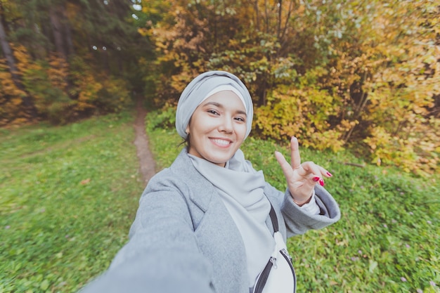 Moda jovem muçulmana asiática em hijab tirando uma selfie em smartphone ao ar livre no parque outono