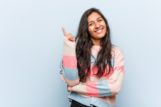 Moda jovem mulher indiana sorrindo alegremente apontando com o dedo indicador fora.