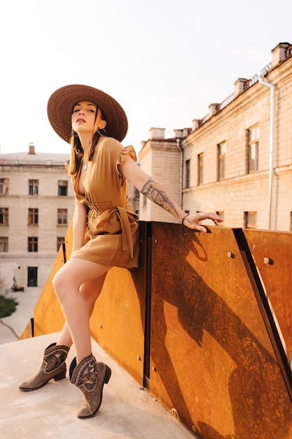 Moda jovem mulher vestida com um vestido de verão com um chapéu largo de vime caminha e posa na cidade velha.