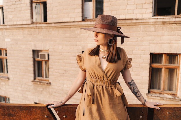 Moda jovem mulher vestida com um vestido de verão com um chapéu largo de vime caminha e posa na cidade velha.