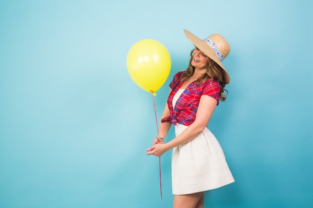 Moda jovem sorridente com balão de ar amarelo sobre fundo azul colorido com copyspace.