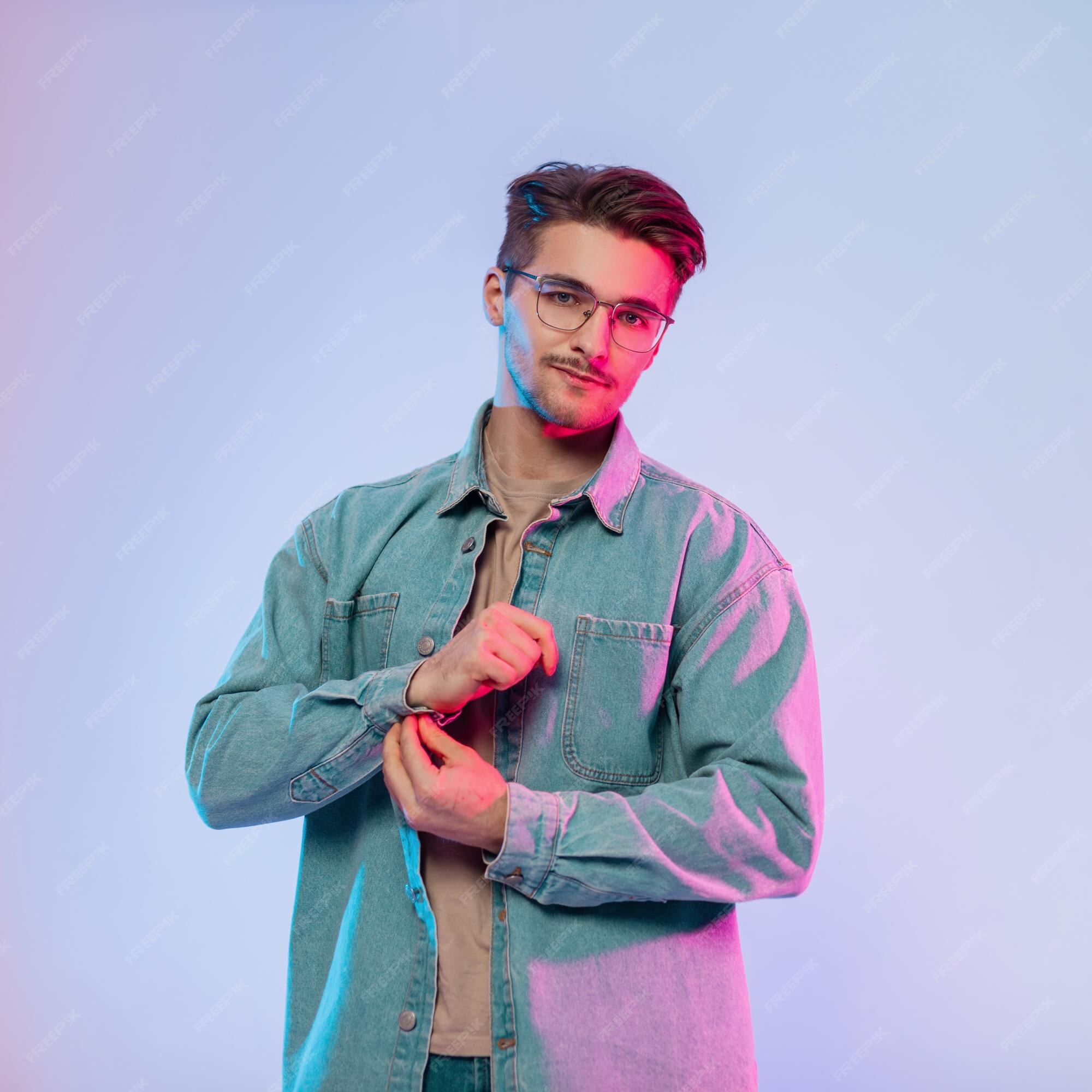 Moda joven y guapo modelo de hombre feliz con peinado y gafas vintage en  traje de mezclilla de moda usa chaqueta de jeans en estudio con luces  azules y rosas | Foto