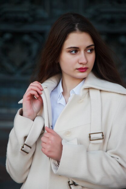 Moda joven hermosa mujer elegante en bata blanca caminando en la calle. Tendencia de la moda de otoño para mujeres sonrientes, felices y decididas. Concepto de estilo, moda, belleza y metas de logro. Copia espacio