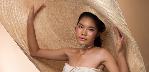 Moda joven mujer asiática delgada ojos de piel bronceada maquillaje hermoso vestido blanco de moda posando atractivo glamour mirada muy grande sombrero de paja. Estudio de iluminación de fondo crema amarillo beige, sol caliente de la playa de verano