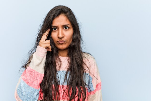 Moda joven mujer india señalando el templo con el dedo, pensando, centrado en una tarea